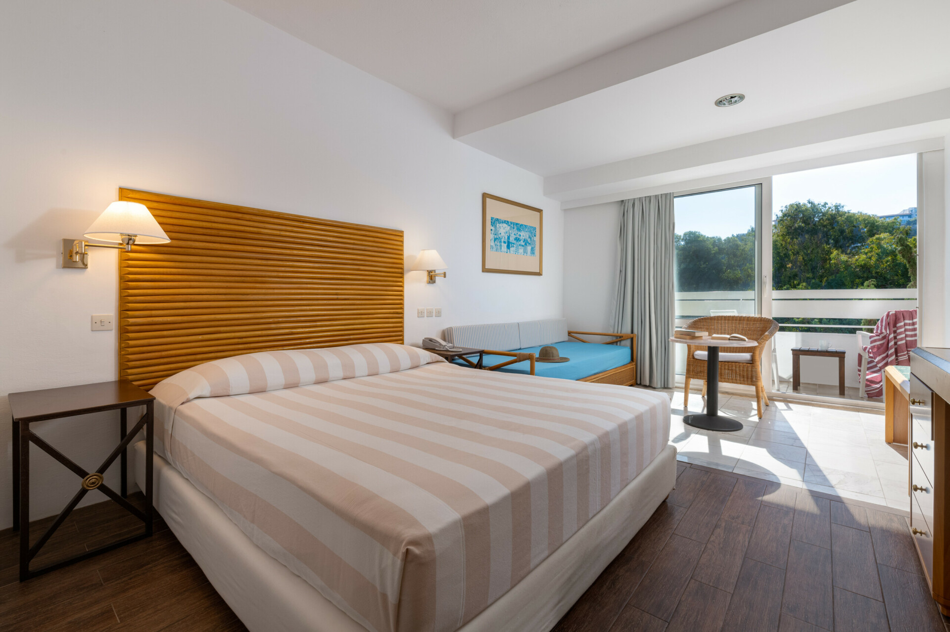 Άνετη εικόνα του τρίκλινου δωματίου στο ξενοδοχείο Dionysos, με ένα διπλό κρεβάτι, έναν μονό καναπέ-κρεβάτι και ιδιωτικό μπαλκόνι με θέα στον κήπο